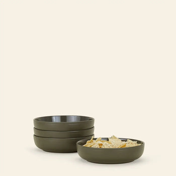 A set of four olive green Hawkins New York Essential Low Bowls is arranged beside a matching bowl filled with tortilla chips, all against a plain light beige background, adding style to any dining setup.