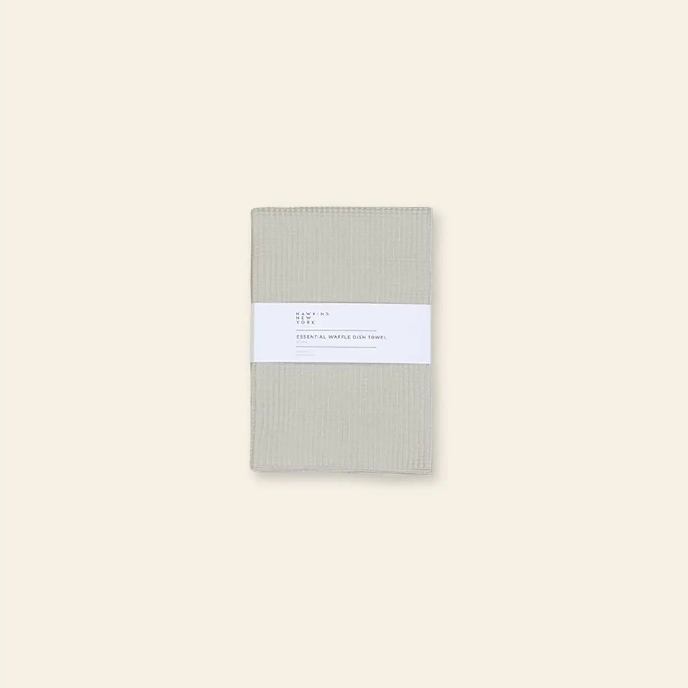 A set of two folded beige Hawkins New York Essential Waffle Dish Towels, wrapped with a white paper label, shown on a light beige background.
