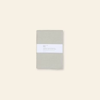 A set of two folded beige Hawkins New York Essential Waffle Dish Towels, wrapped with a white paper label, shown on a light beige background.