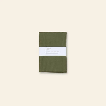 A pair of olive green Hawkins New York Essential Waffle Dish Towels, neatly folded with a white paper band, are displayed against a plain beige background.