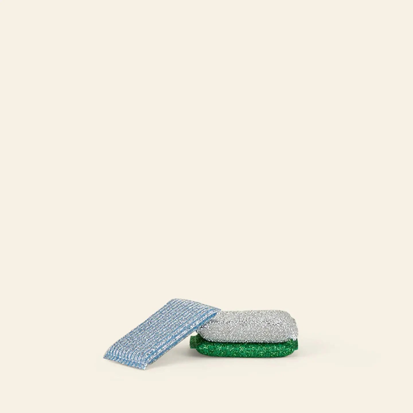 A set of three Hawkins New York Lurex Sponges sits on a simple beige background—one features green and silver tones, while a blue and white scrubbing pad rests beside it.