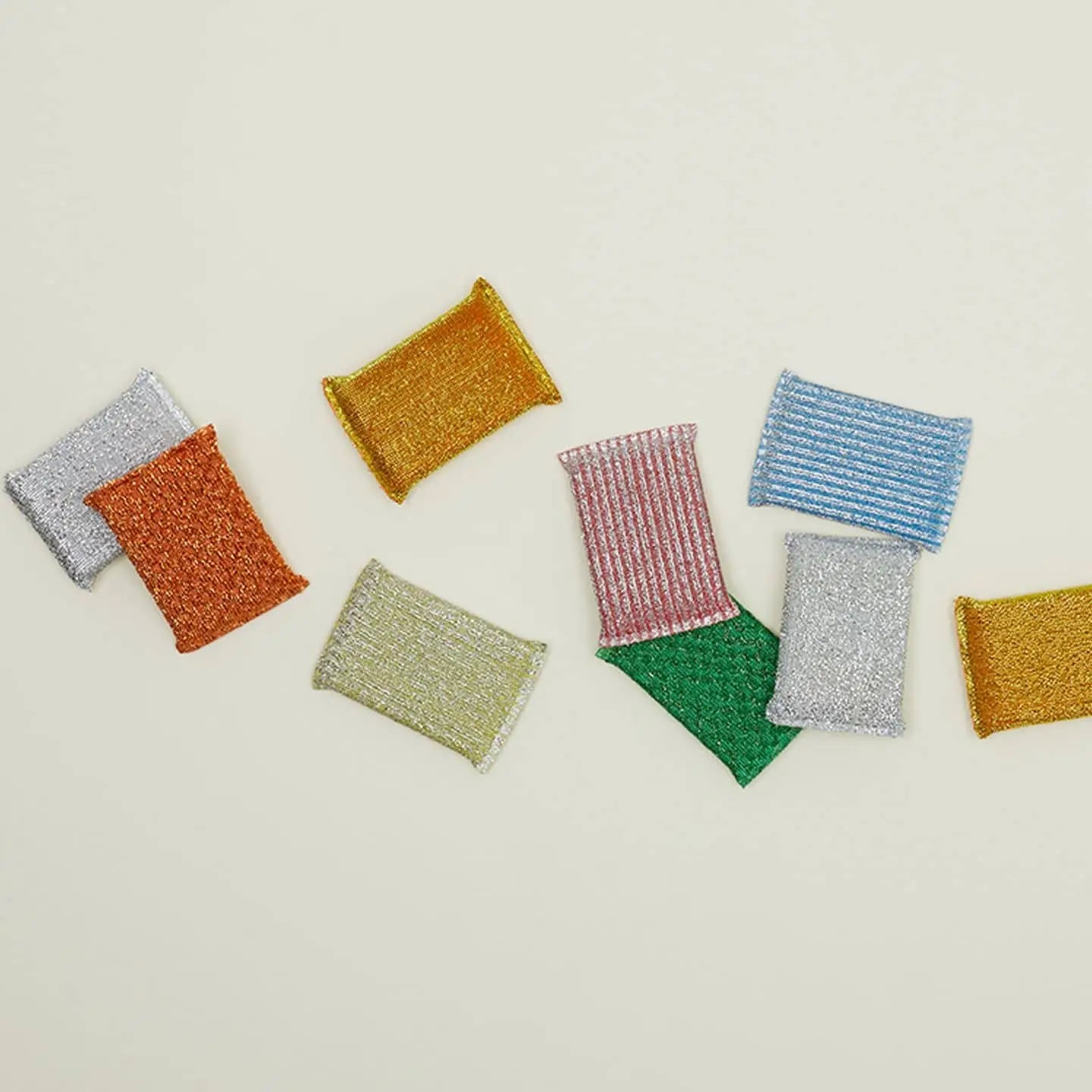 A set of three colorful Hawkins New York Lurex Sponges, featuring vibrant metallic designs, is arranged on a light beige surface—stylish and durable high-quality sponges for any kitchen cleanup.