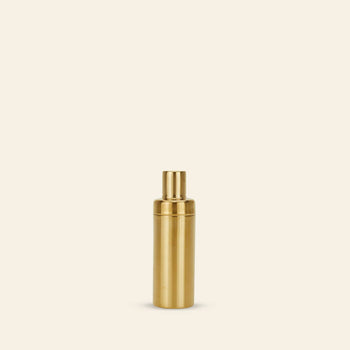 A gold metallic spray bottle stands upright on a beige background, echoing the sleek design of the Hawkins New York Simple Cocktail Shaker.