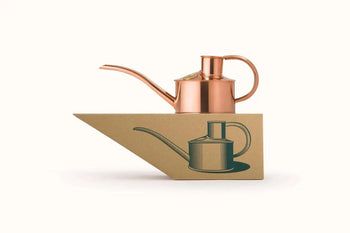 The Haws The Fazeley Flow One Pint watering can sits atop a geometric cardboard piece with a black watering can illustration, set against a plain white background.