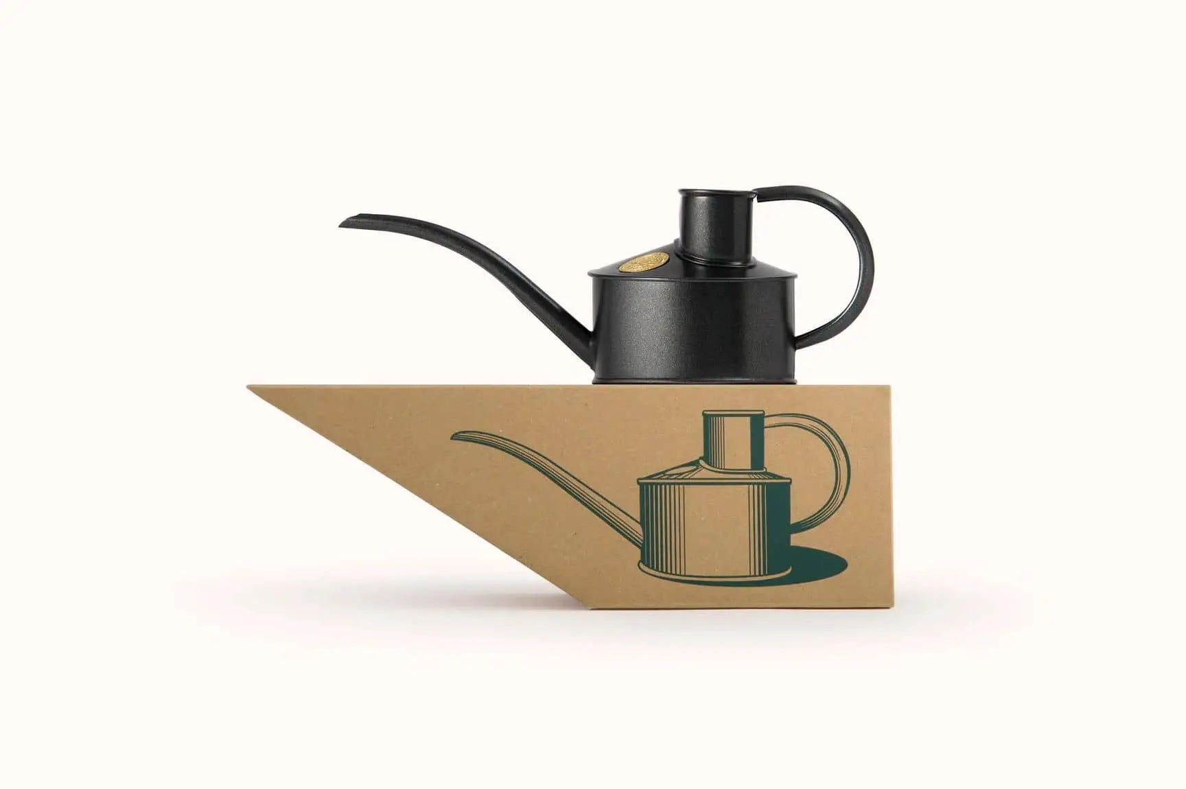The Haws The Fazeley Flow One Pint watering can in black sits atop a triangular box featuring a green illustration of the can, with both set against a plain white background.