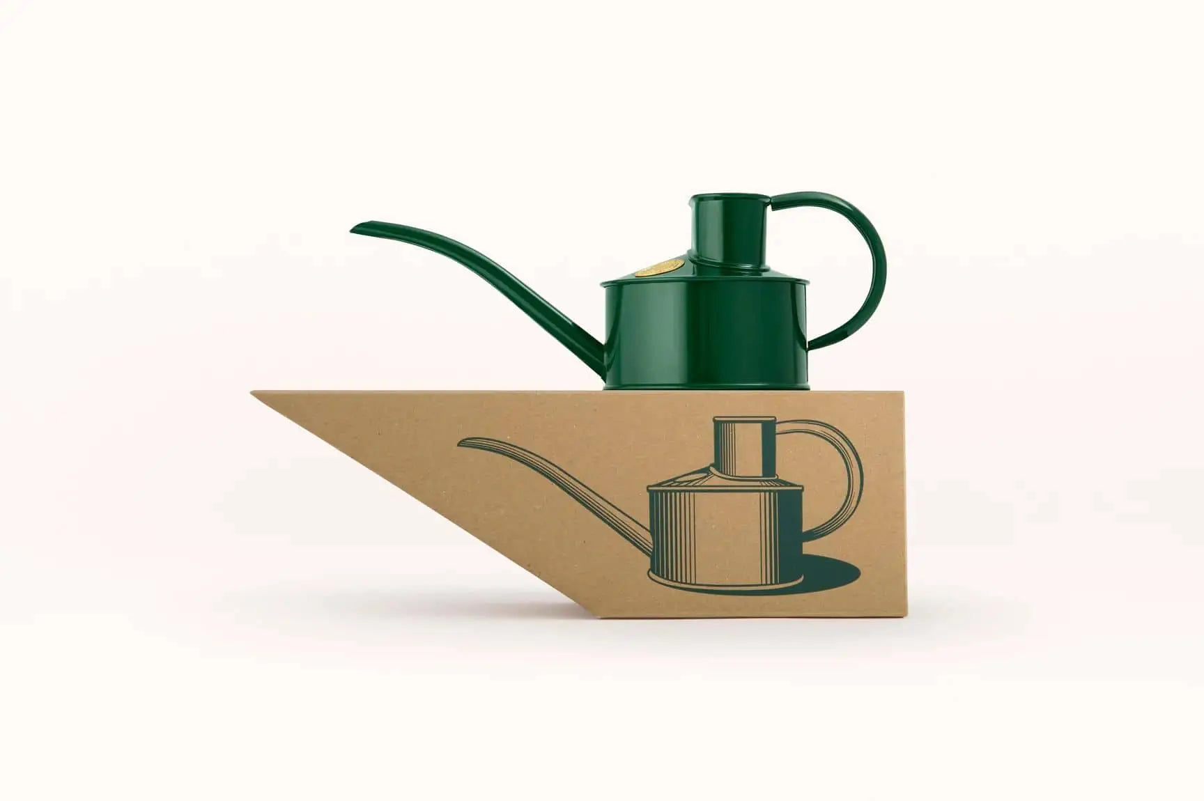 The Haws The Fazeley Flow One Pint watering can by Haws, in green, rests on a brown triangular box with a matching tool illustration, all set against a plain white background.