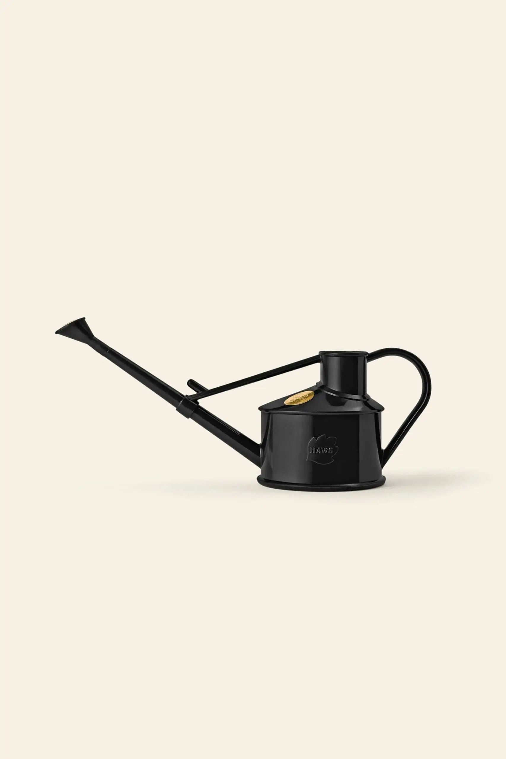 The Haws The Langley Sprinkler, a black metal watering can with an adjustable head, long spout, and curved handle from Haws, is placed on a plain light beige background.