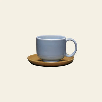 The Hübsch Amare Cup With Saucer by Hübsch features a retro-inspired light blue ceramic cup paired with a round brown saucer, set against a plain light beige background.