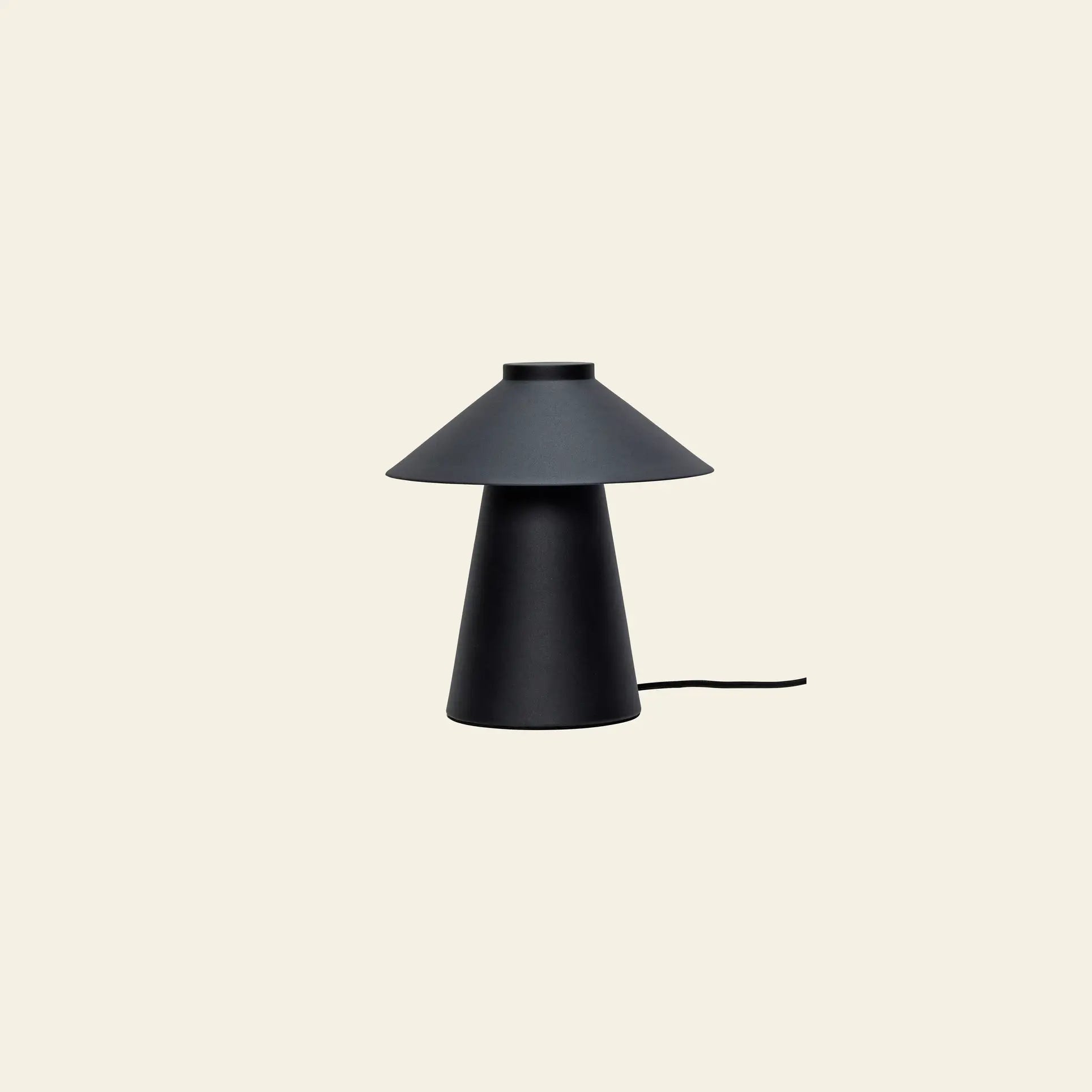 The Hübsch Chipper Table Lamp by Hübsch features a modern black design with a conical base and wide, flat shade. Positioned on a light beige background, it enhances ambiance while its power cord extends from the base.