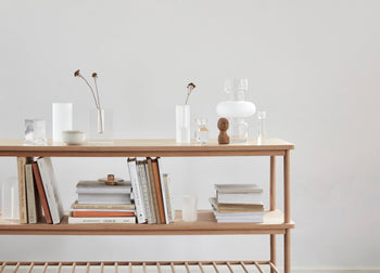 A minimalist wooden shelf against a plain light wall, styled with stacked books, elegant glassware, vases of dried flowers, a small wooden figurine, and a Hübsch Clay Bowls Set of 2 for refined charm.