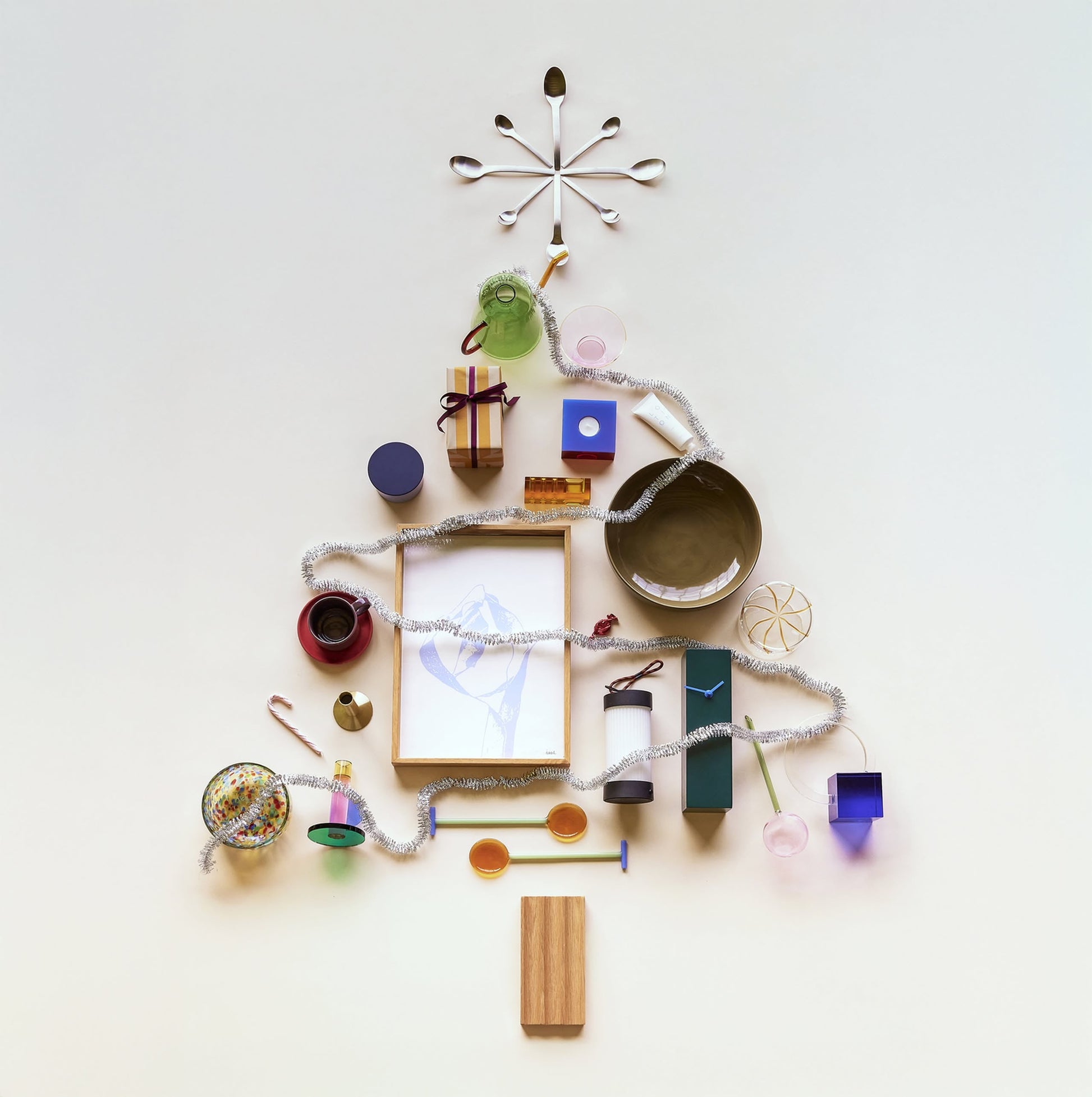 A Christmas tree made from household items—cups, bowls, boxes, and the Hübsch Hour Clock by Hübsch—topped with tinsel as garland and artfully arranged on a light background.