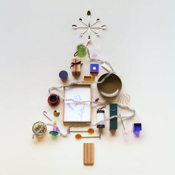 A Christmas tree made from household items—cups, bowls, boxes, and the Hübsch Hour Clock by Hübsch—topped with tinsel as garland and artfully arranged on a light background.