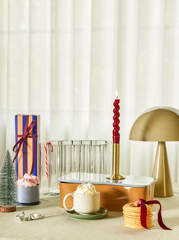 A festive table showcases the Hübsch Mush Table Lamp Mini by Hübsch, a mug of whipped cream-topped hot chocolate, waffle cookies, wrapped gifts in various colors, a red candle, a candy cane, and mini Christmas trees—ideal for the modern home.
