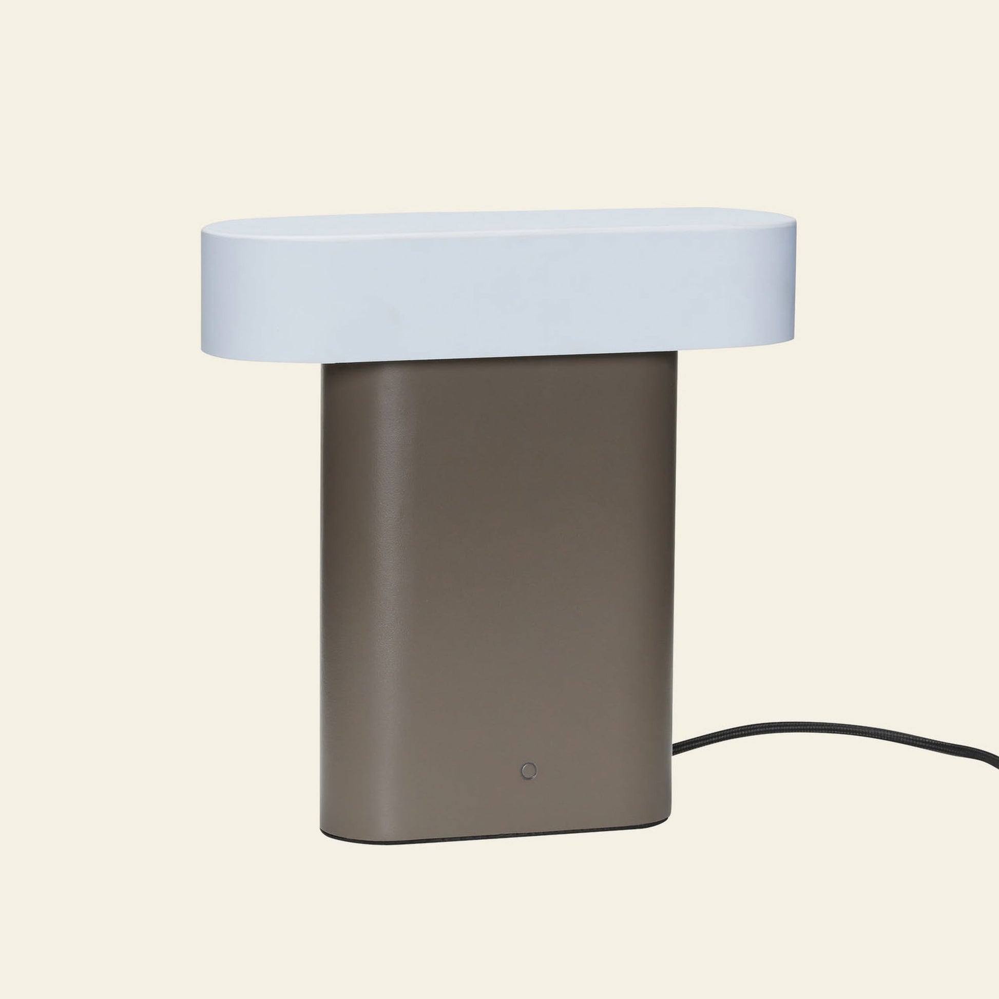 The Hübsch Sleek Table Lamp by Hübsch features a rectangular brown base, a flat oval white top, and a black power cord, creating a modern minimalistic look against a plain background.