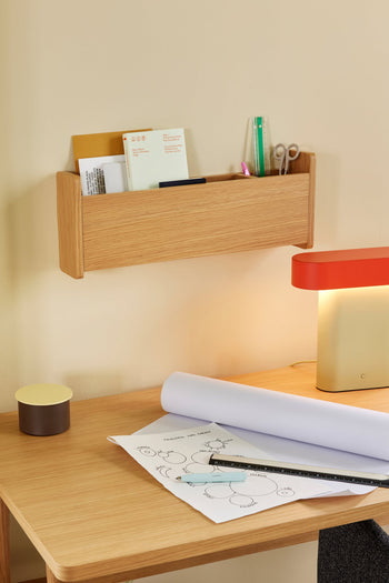 A wooden desk with architectural drawings, a ruler, and the Hübsch Sleek Table Lamp (dimmable). Above, a wooden wall organizer holds papers, scissors, pencils, and a green ruler. A modern minimalist look is finished with a small round container.
