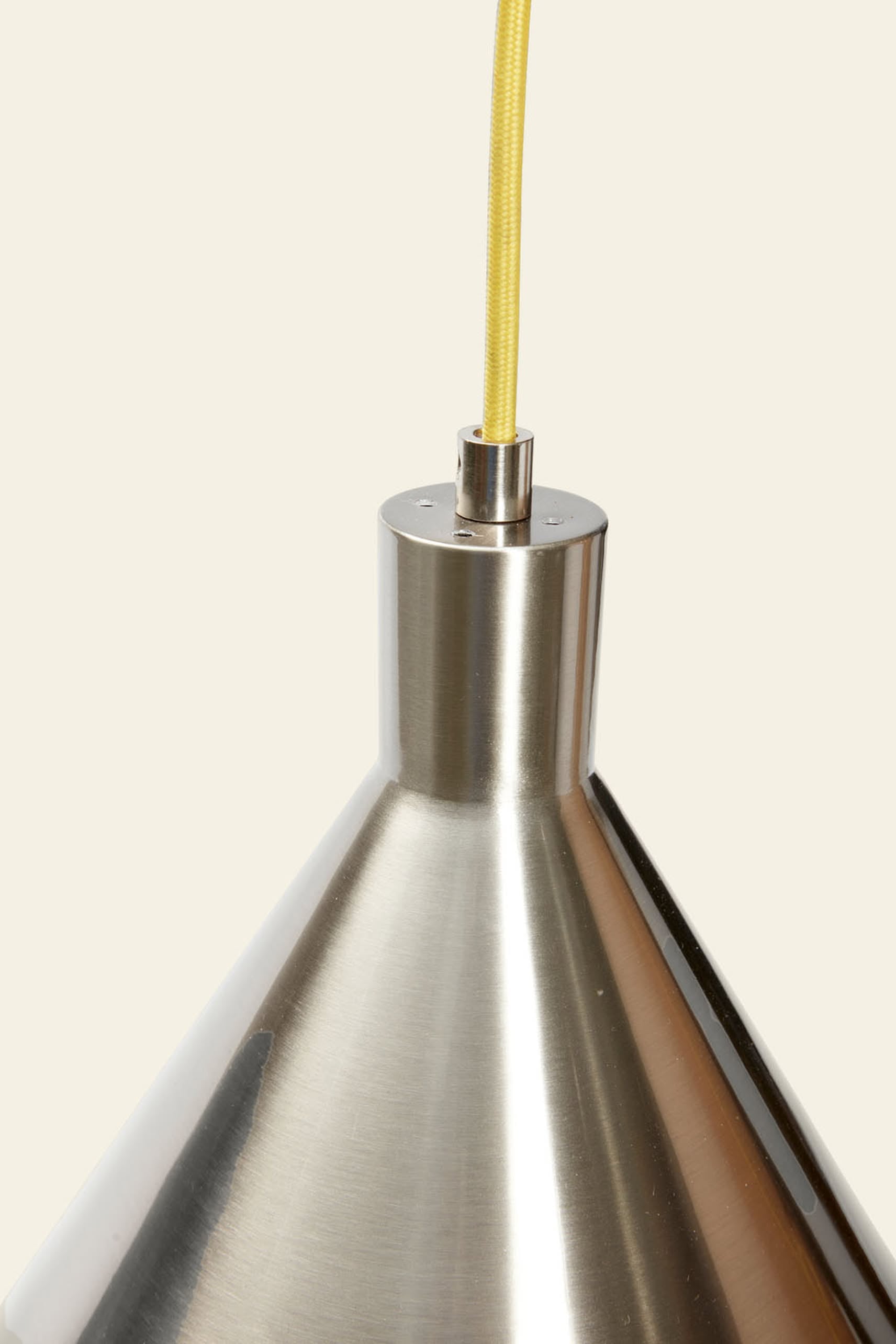 Close-up of the Hübsch Yama Pendant—a metallic, cone-shaped light by Hübsch featuring a shiny finish and yellow cord—shown against a plain light background.