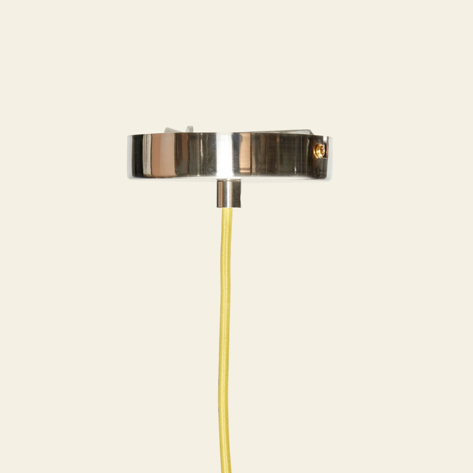 The Hübsch Yama Pendant by Hübsch features a modern wall-mounted design with a metallic base and yellow cord, hanging vertically against a light beige background for an elegant, contemporary look.