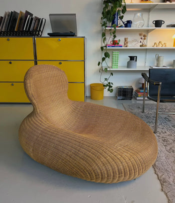 The IKEA Rattan Storvik Lounge Chair brings vintage charm to a modern room with IKEA yellow cabinet drawers, a desk, books and decor on shelves, and a hanging plant.
