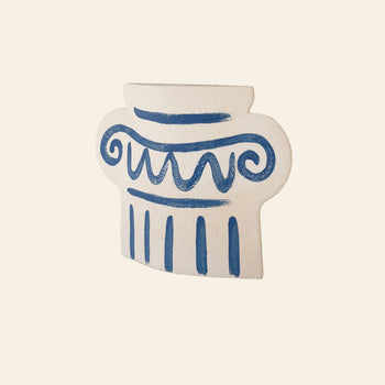 The INI CERAMIQUE Greek Column Ceramic Vase is a flat, white handcrafted vase with blue scroll and vertical line details, inspired by ancient Greek columns. Shown against a light beige background.
