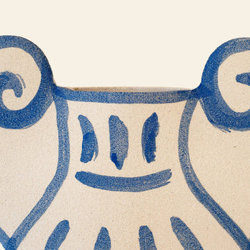A close-up of the INI CERAMIQUE Krater N°1 Ceramic Vase shows beige ceramic with blue painted lines forming a smiling face and spiral shapes, echoing Greek pottery in a contemporary, playful design by INI CERAMIQUE.