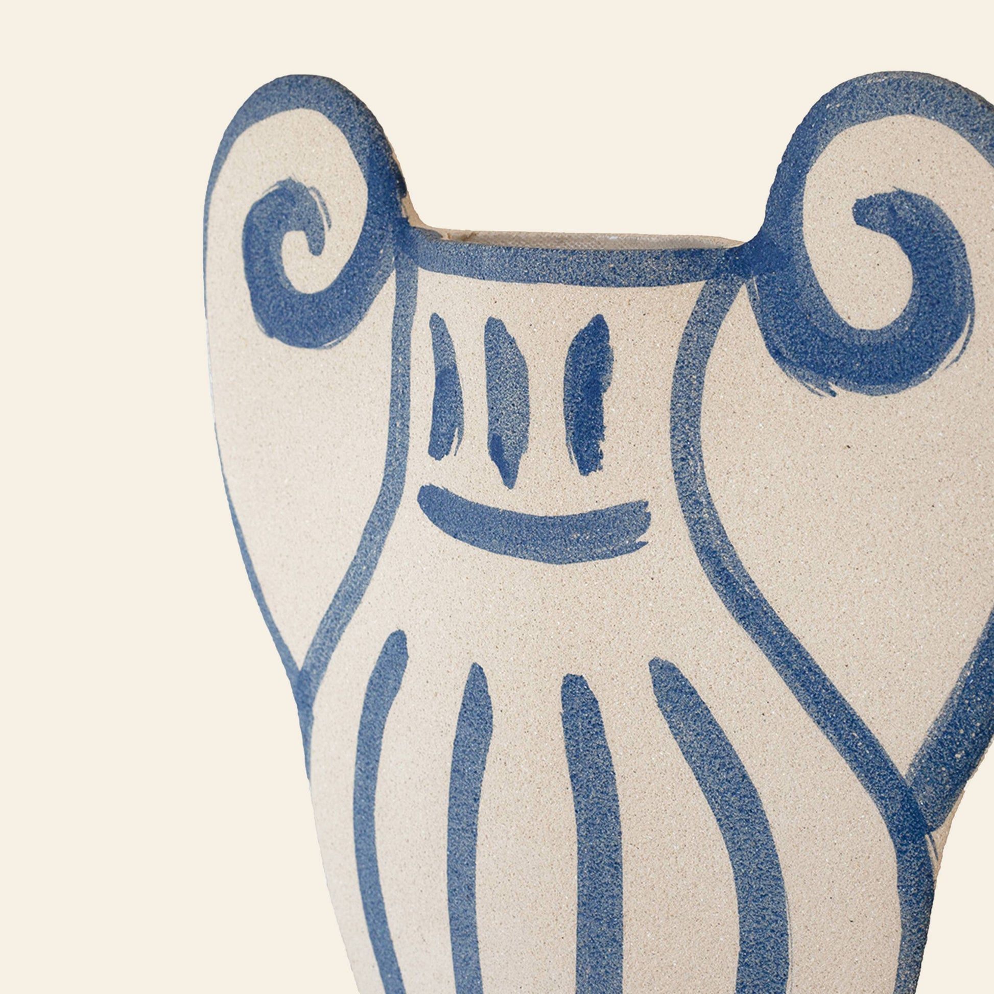 The INI CERAMIQUE Krater N°1 Ceramic Vase features a cream base with blue painted designs—smiling face and swirls—blending Greek pottery influences with modern style, all set against a light beige background.