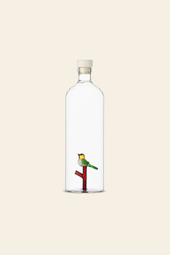The Ichendorf Milano Animal Farm Bottle by Ichendorf Milano features a handcrafted glass design with a white cap, showcasing a small bird on a red and green branch inside, set against a plain light beige background.