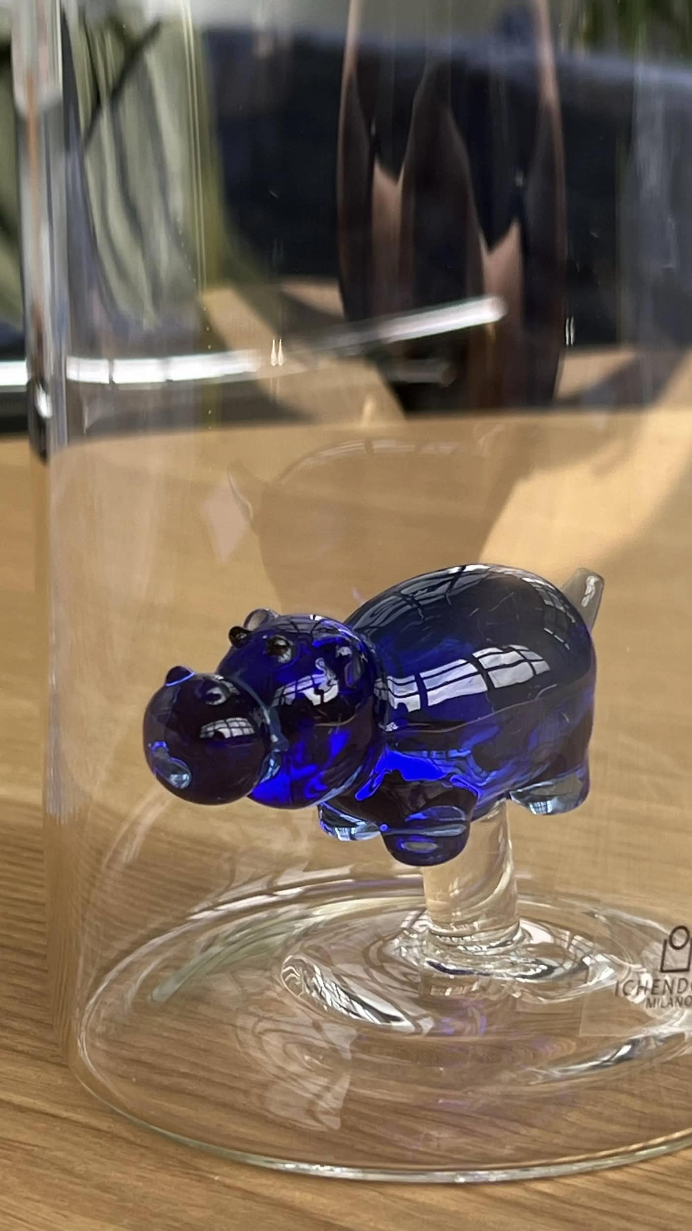 The Ichendorf Milano Animal Farm Bottle by Ichendorf Milano is showcased on a wooden surface, resting on a clear glass stand and protected by a transparent glass cover.