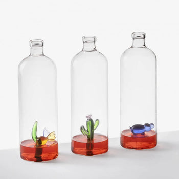 Three Ichendorf Milano Animal Farm Bottles by Ichendorf Milano, featuring handcrafted glass sculptures—a flower, a cactus, and a blue animal—sit on a white background with red liquid at the base.