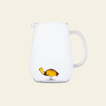 The Ichendorf Milano Animal Farm Pitcher - Amber Turtle is a clear hand-crafted glassware pitcher with a handle, featuring a small amber glass turtle figurine at the bottom. It’s part of the charming Animal Farm collection by Ichendorf Milano.