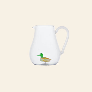 The Ichendorf Milano Animal Farm Pitcher - Duck from Stacked Store is a clear glass pitcher featuring a small, colorful duck figurine inside, displayed against a plain light beige background.
