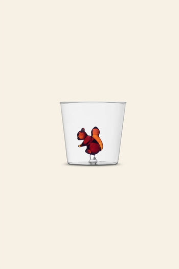 The Ichendorf Milano Animal Farm Tumbler by Ichendorf Milano rests on a light beige surface, featuring red and orange liquid swirling at the bottom in an abstract, flower-like shape.