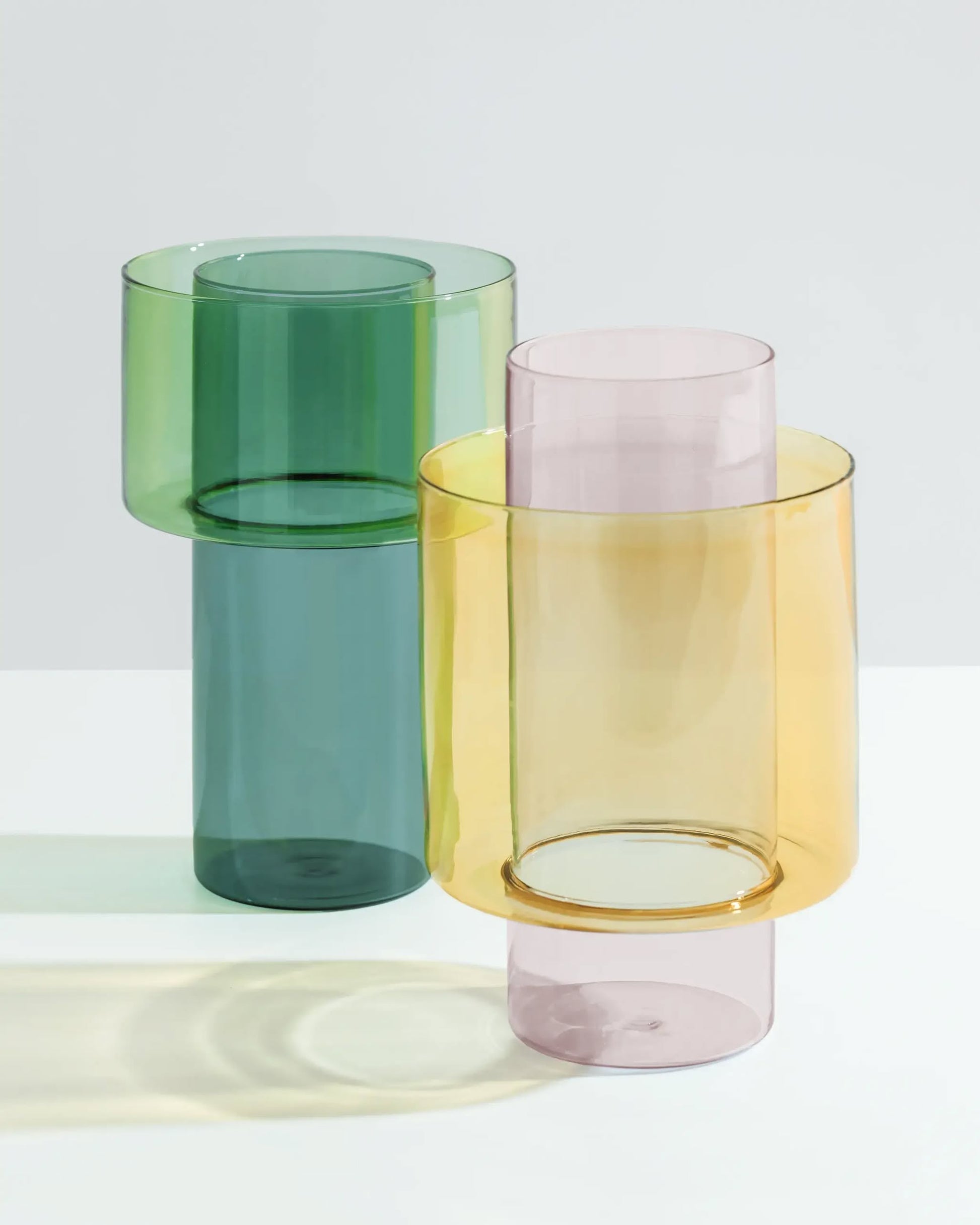 The Ichendorf Milano Boreale Vase A set by Ichendorf Milano includes two modern cylindrical borosilicate vases—one green and one pink with yellow tint—featuring geometric shapes, perfect for creative floral displays on any surface.