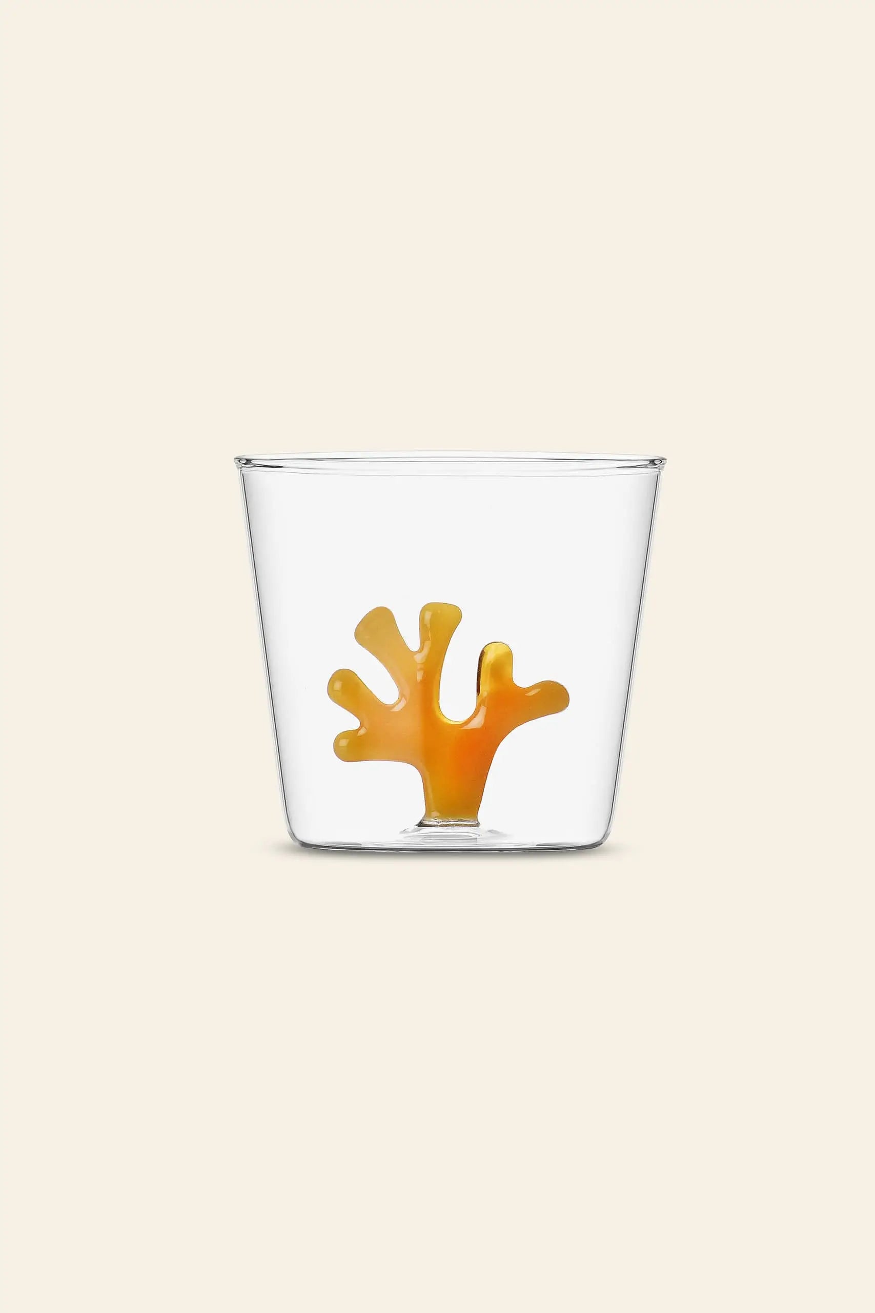 The Ichendorf Milano Coral Reef Tumbler features a clear glass design with an orange coral motif by Alessandra Baldereschi, inspired by vibrant underwater ecosystems, shown here against a plain beige background.