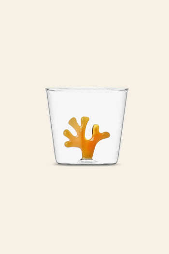 The Ichendorf Milano Coral Reef Tumbler features a clear glass design with an orange coral motif by Alessandra Baldereschi, inspired by vibrant underwater ecosystems, shown here against a plain beige background.