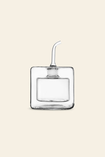 The Ichendorf Milano Cube Square Doublewalled Oil Bottle by Ichendorf Milano, with its clear, square design and curved spout, is elegantly displayed on a light beige background—combining modern style and smart function for olive oil storage.