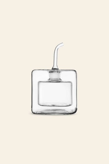 The Ichendorf Milano Cube Square Doublewalled Oil Bottle by Ichendorf Milano is a handcrafted, clear, square kitchenware piece with a short angled spout for olive oil, displayed on a plain beige background.