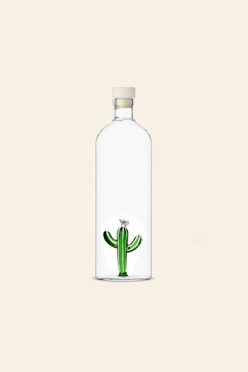 The Ichendorf Milano Desert Plants Bottle by Ichendorf Milano features a clear glass bottle with a beige cap, housing a small green cactus with a pink flower, set against a light beige background—a delightful desert-themed decor piece.
