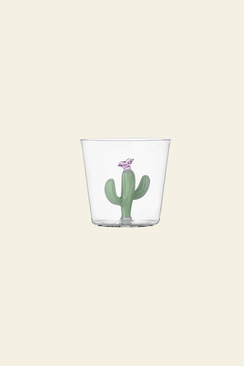 The Ichendorf Milano Desert Plants Tumbler is a clear glass cup from the Ichendorf Milano collection, featuring a small green cactus motif and a purple bird figurine inside, displayed against a plain beige background.