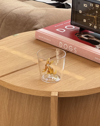 The Ichendorf Milano Dogs Tumbler - Chihuahua by Ichendorf Milano, featuring a tiny Chihuahua inside, sits on a wooden table beside a red book titled DOGS and a black clock.