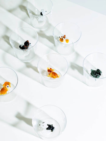 Seven Ichendorf Milano Dogs Tumblers - Chihuahua by Ichendorf Milano are arranged on a white surface, each containing a small animal figurine like a fox, bear, panda, or Chihuahua, viewed from above with soft shadows on the table.
