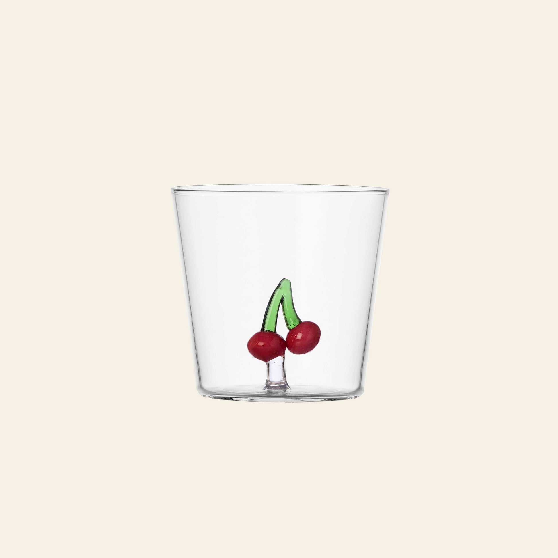 The Ichendorf Milano Fruits and Flowers Tumbler by Ichendorf Milano is a clear glass featuring a small, hand-painted design of two red cherries with green stems near the base, set against a light beige background.