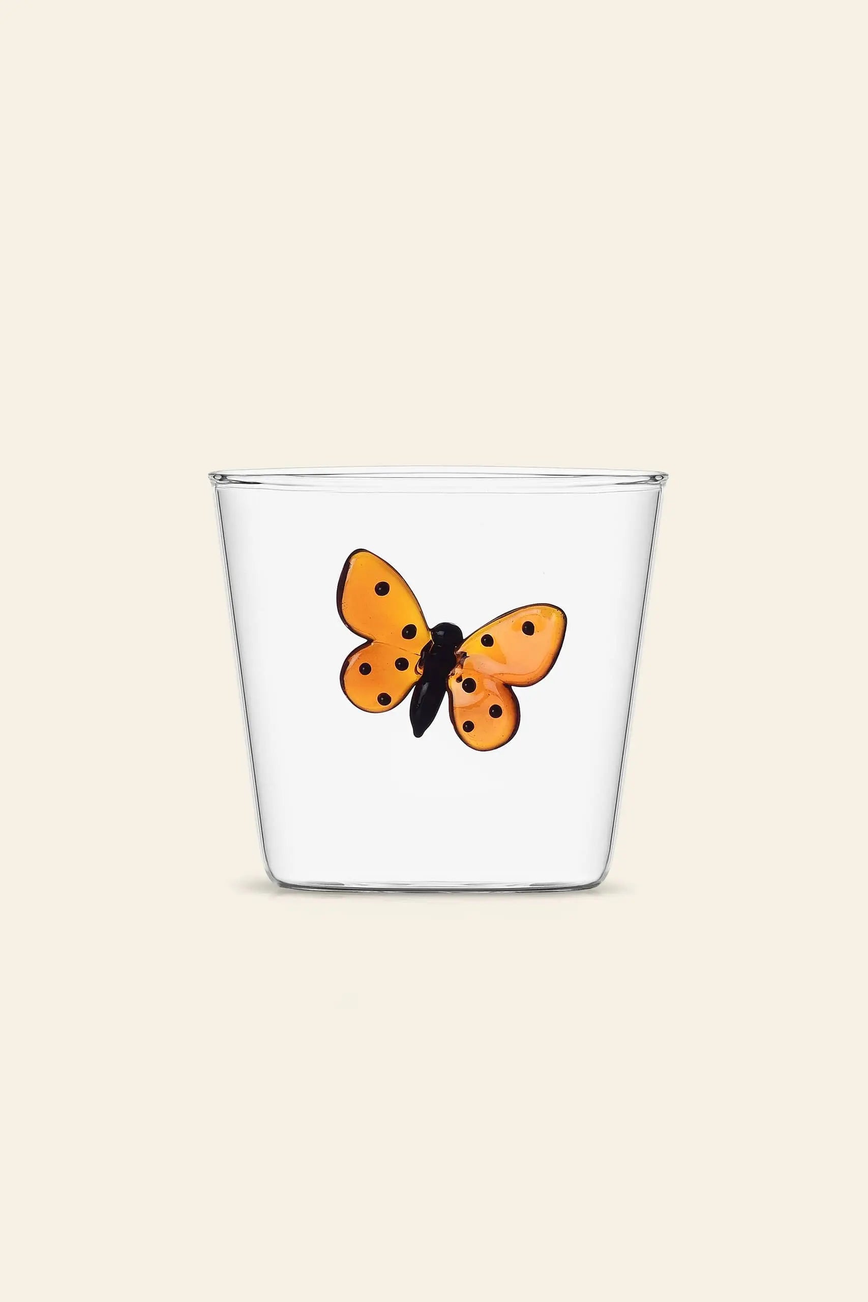 The Ichendorf Milano Garden Picnic Tumbler by Ichendorf Milano is a clear glass cup with an orange and black butterfly motif on the front, set against a plain beige background—ideal for adding charm to your next garden picnic.