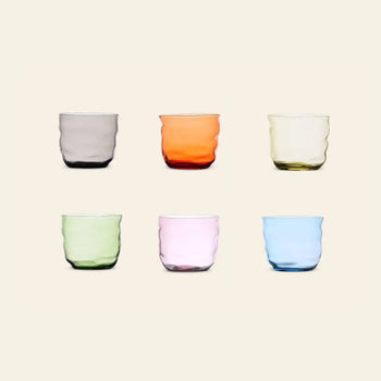 The Ichendorf Milano Poseidon Tumbler Set of 6 features organically shaped, colorful glasses—gray, orange, yellow, green, pink, and blue—arranged in two rows of three on a plain light background.