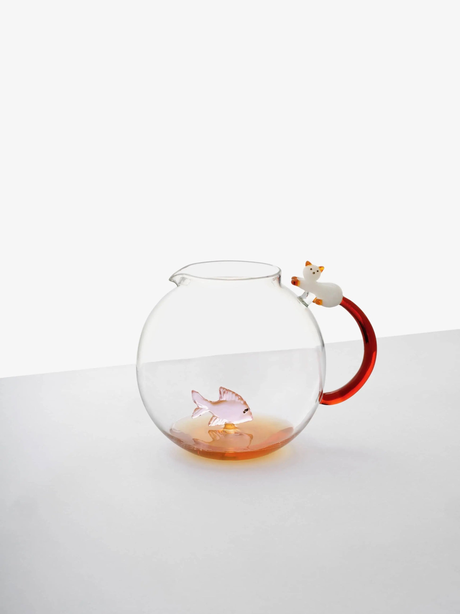 The Ichendorf Milano Tabby Cat Jug features a clear fishbowl shape, red handle, white cat figurine on top, and includes a pink glass fish with an amber tail inside.