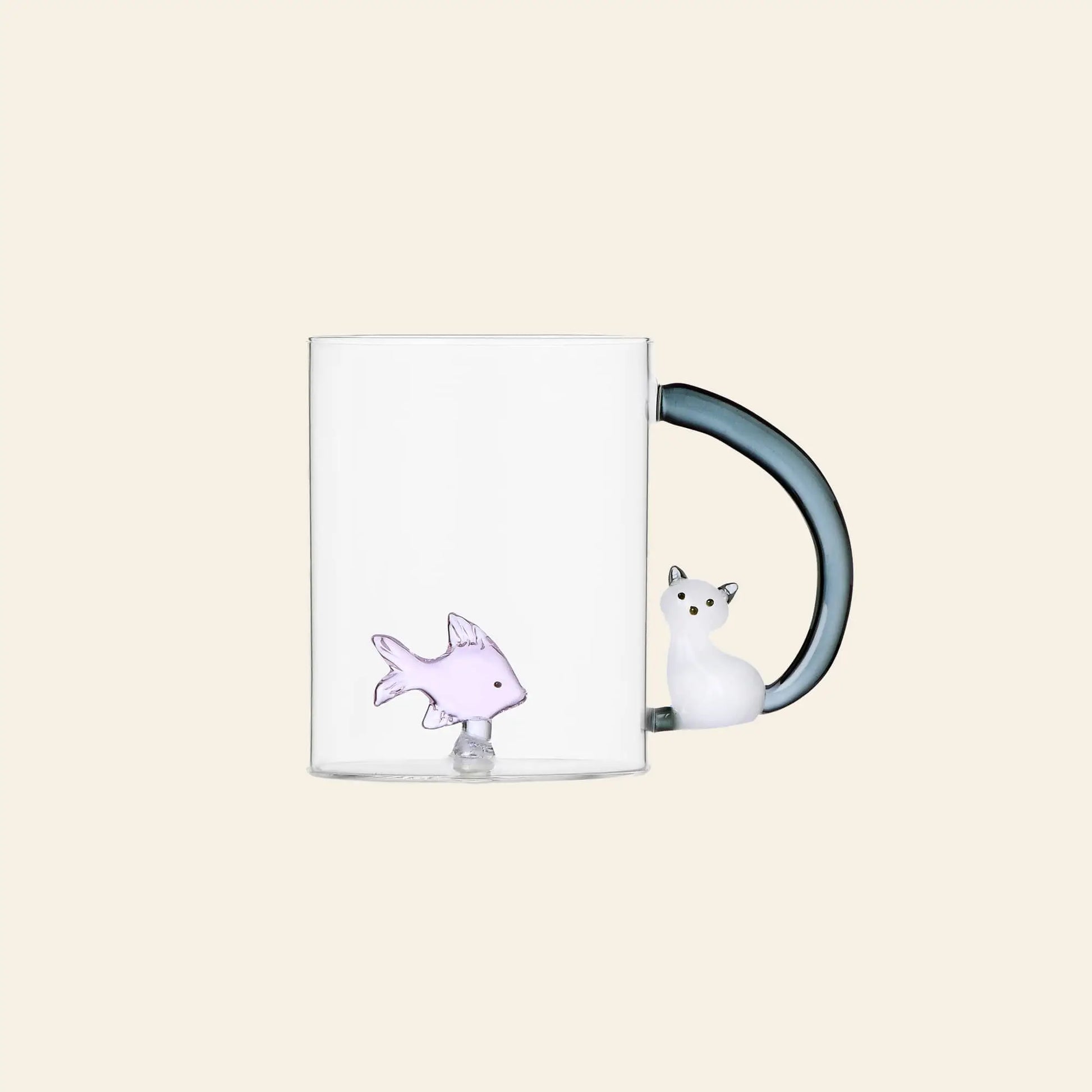 The Ichendorf Milano Tabby Cat Mug by Ichendorf Milano is a clear handcrafted mug with a small purple fish figurine at the bottom and a dark cat-shaped handle featuring the cat’s head and paws. Perfect for cat figurine fans. Background is off-white.