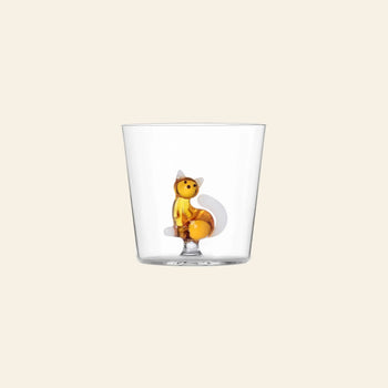 The Ichendorf Milano Tabby Cat Tumbler, by Ichendorf Milano, is a clear glass cup featuring a small upright orange fox figurine at the center, ideal for cat lovers and displayed on a plain beige background.