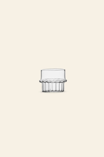 The Ichendorf Milano Transit Coffee Cup by Ichendorf Milano features a clear, hand-crafted glass design with a wide rim and ribbed base, showcased on a light beige background to highlight its distinctive style.