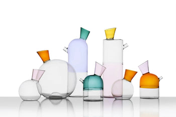 A collection of Ichendorf Milano Travasi Oil Bottles in various geometric designs and sizes, each featuring a tilted, vibrant spout, arranged on a reflective surface with a white background.