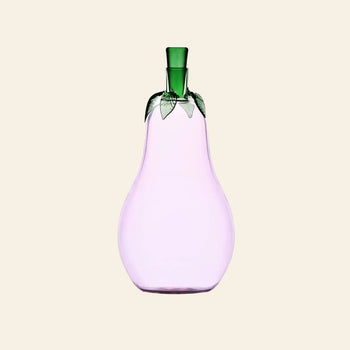 The Ichendorf Milano Vegetables Bottle by Ichendorf Milano is a handcrafted glass bottle shaped like a pear, with a light purple body and green leaf-like top, making it a charming decorative piece against a beige background.