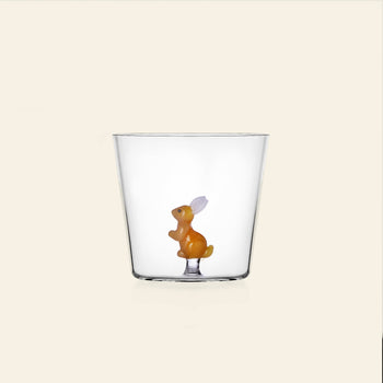 The Ichendorf Milano Woodland Tales Tumbler by Ichendorf Milano is a clear glass featuring a small orange rabbit with white ears at its base, displayed on a plain, light beige background.